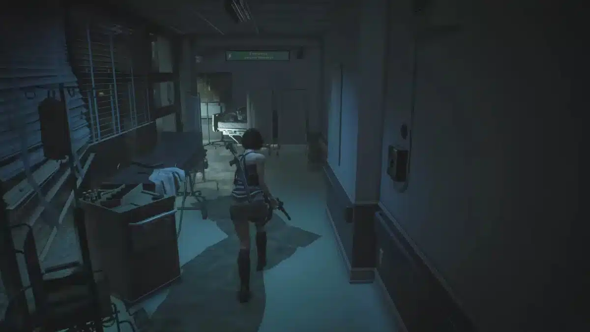 Jill Valentine in a striped tank top and shorts walks down a dimly lit hospital corridor holding a weapon.