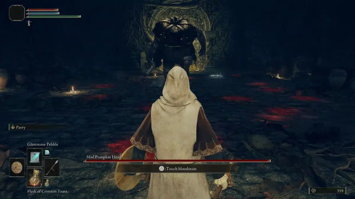 First-person perspective of a player character wearing a hooded robe, facing a large, grotesque, pumpkin-headed enemy in a dimly lit dungeon. The player has a shield and is preparing to fight, with game UI elements visible, including health and stamina bars, and item selection.