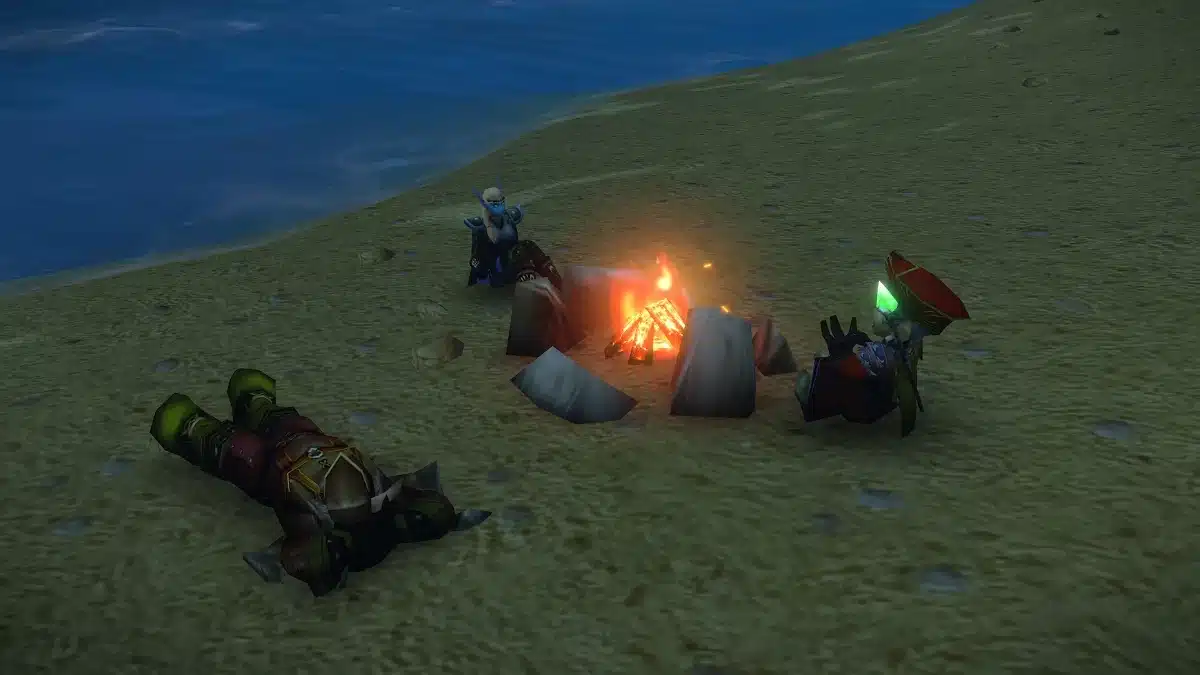 Three figures sit around a campfire on a sandy shore next to a body of water. One figure, lying on its back with its arms and legs spread, is green-skinned with rough armor. Two other figures, one seated and dressed in blue armor and the other seated in ornate red and blue robes with a red hat and a green gem, are near the campfire.